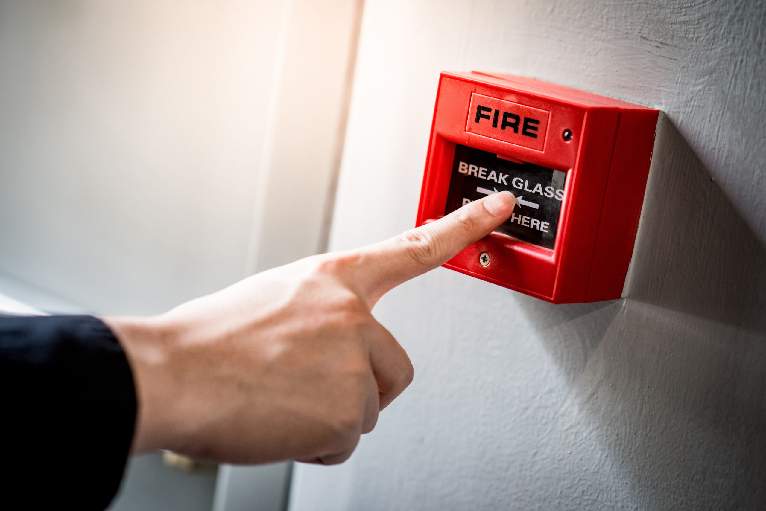 Male hand pointing at red fire alarm switch Male hand pointing at red fire alarm switch on concrete wall in office building. Industrial fire warning system equipment for emergency.